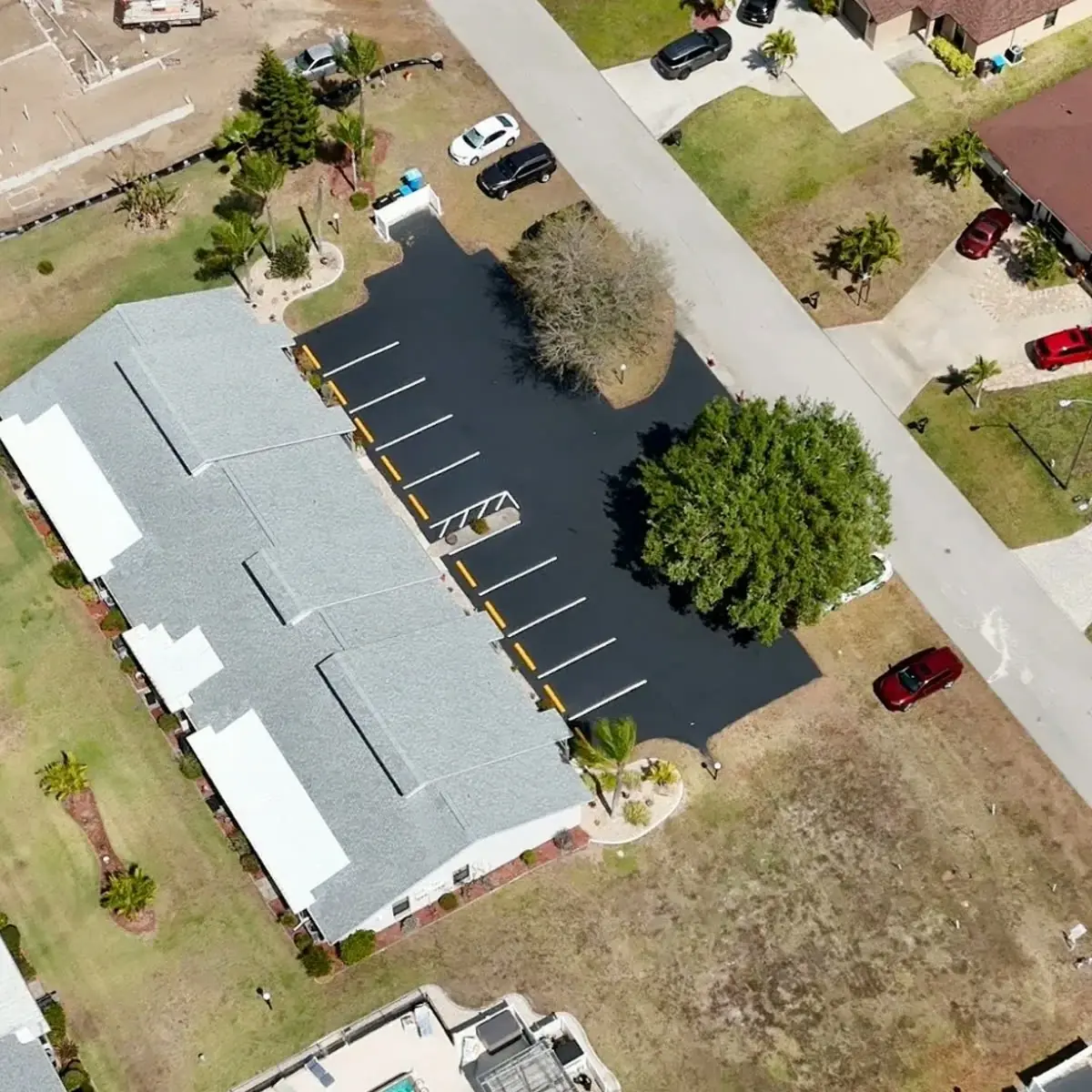 Aerial view of a freshly sealcoated community building parking lot with new striping and yellow curbing in Cape Coral Florida by Florida Sealcoat and Striping